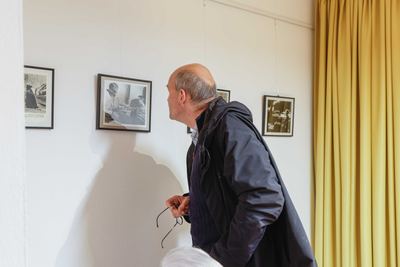 Ein Besucher mit Brille in der Hand betrachtet gerahmte Schwarzweiß-Aushangfotos mit Schachszenen neben einem gelben Vorhang