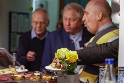 Gäste bedienen sich am Buffet mit belegten Häppchen, im Vordergrund gelbe Rosen und Wasserflaschen auf der Theke