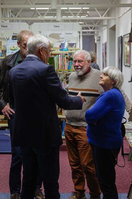 Vier Gäste im Gespräch zwischen Kinderbuchregalen der Abteilung „Tiere“, ein Herr im Sakko gestikuliert zu einem Paar in Pullovern