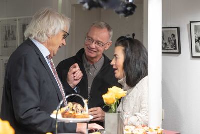 Drei Gäste im Gespräch am Buffet mit gelben Rosen, an der Wand gerahmte Schwarz-Weiß-Filmfotos mit Schachszenen