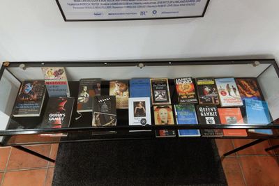 Glasvitrine mit Schachromanen und Taschenbüchern zum Thema Schach, darüber ein gerahmtes Filmplakat der Ausstellung „Schach und Film“