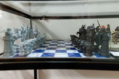 Seitlicher Blick auf ein blau-weißes Sammlerschachbrett mit hellen und dunklen Fantasy-Figuren in Grundaufstellung hinter Glas