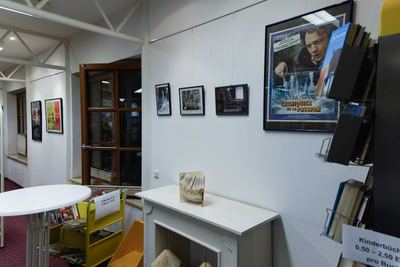Ausstellungsecke in der Stadtbücherei mit großem gerahmtem Kinoplakat zum Schachfilm, kleinen Filmfotos und einem Buchkunstobjekt