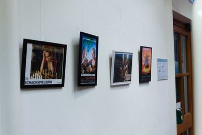 Gerahmte Filmplakate und Szenenbilder mit Schachspielerinnen und Schachbrettern an einer weißen Wand der Stadtbücherei