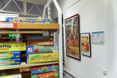 Regal mit Gesellschaftsspielen im Vordergrund, dahinter zwei gerahmte historische Kinoplakate an der Wand der Bücherei