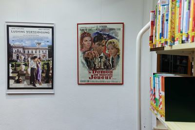 Zwei Filmplakate mit Schachmotiven: Paar zwischen übergroßen Gartenschachfiguren und gemaltes Plakat mit Spieler vor Figuren