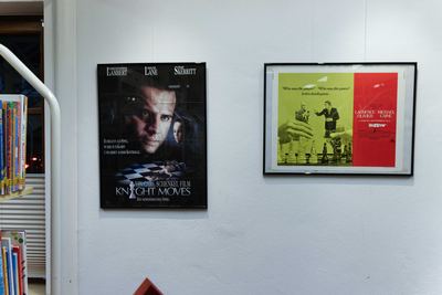 Dunkles Thriller-Plakat mit Schachbrett und grün-rotes Filmplakat mit Spielern zwischen Schachfiguren, gerahmt an weißer Wand