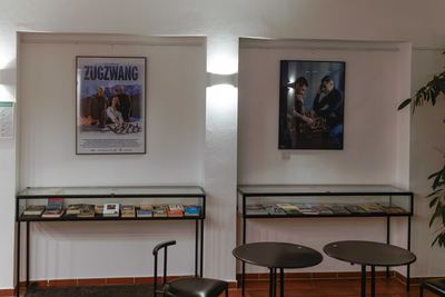 Zwei beleuchtete Wandnischen mit großen Filmplakaten zum Schach, darunter Glasvitrinen mit Büchern und vorne Bistrotische