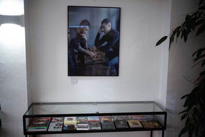 Großformatiges Foto zweier Männer beim Schachspiel auf einem Koffer, darunter eine Vitrine mit Schachfilmen auf DVD