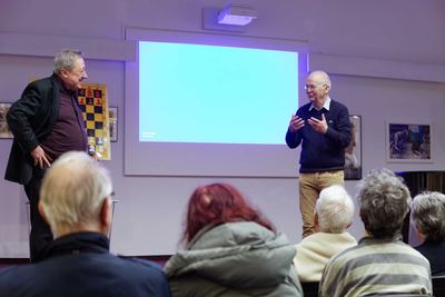 Moderator und Großmeister im Gespräch vor dem Publikum, einer neben dem Demobrett, der andere gestikulierend vor der Leinwand