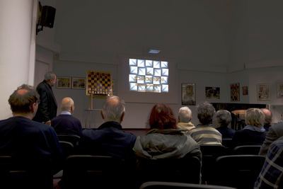 Abgedunkelter Saal: Titelfolie zum Vereinsjubiläum der Schachunion Ebersberg-Grafing auf der Leinwand, daneben das Demobrett