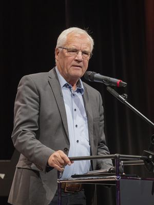 Älterer Redner mit Brille und grauem Sakko spricht am Rednerpult ins Mikrofon