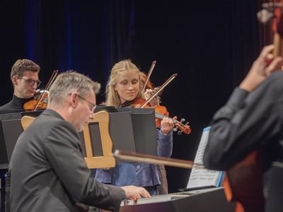 Pianist am Digitalpiano, dahinter junge Geigerinnen und Geiger des Orchesters, rechts angeschnitten ein Cellist