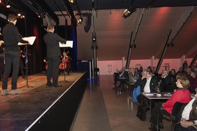 Seitenblick auf das Streicherensemble am Bühnenrand, rechts im Saal das aufmerksam zuhörende Publikum