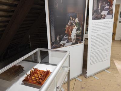 Bernsteinschachspiel in einer Tischvitrine vor Ausstellungstafeln mit einem Genregemälde eines Paares beim Schachspiel
