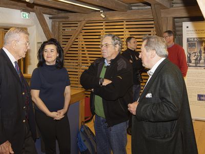 Gäste im Gespräch im Ausstellungsraum mit Holzbalken, rechts ein Ausstellungsbanner zu einer Schallplatte
