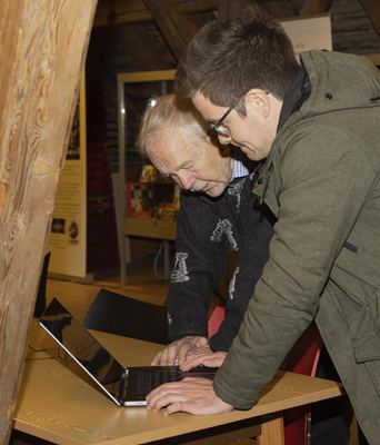 Zwei Besucher beugen sich gemeinsam über einen Laptop im Ausstellungsraum unter dem Dachgebälk