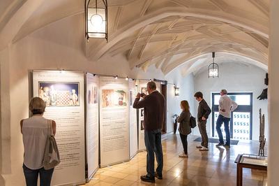 Besucher lesen die Roll-up-Tafeln der Ausstellung „Schach und Religion“ im gewölbten Rathausgang, ein Mann fotografiert eine Tafel