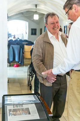 Zwei Männer begrüßen sich mit Handschlag im Rathausflur, vorn ein aufgeschlagener Ordner mit Zeitungsausschnitten