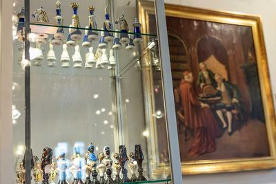 Vitrine mit Porzellan-Schachfiguren vor einem Ölgemälde, auf dem ein Geistlicher in Rot mit zwei Herren an einem Tisch sitzt