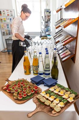 Buffet nach der Eröffnung: Häppchen auf Holzbrettern, Säfte, Wasser und Wein, eine Servicekraft schenkt Gläser ein
