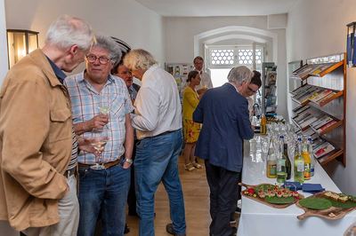Gäste mit Weingläsern am Buffettisch im Rathaus, rechts ein Wandregal mit Broschüren und Prospekten