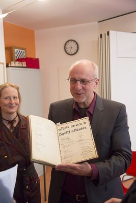 Mann mit Brille zeigt ein aufgeschlagenes altes Gästebuch mit Unterschriften zur 14. Partie vom 8.5.1934 im Bayerischen Hof in München