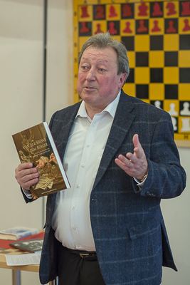 Redner hält das Buch „Von der Krone zum Bürger“ hoch, hinter ihm ein großes gelb-schwarzes Wandschachbrett