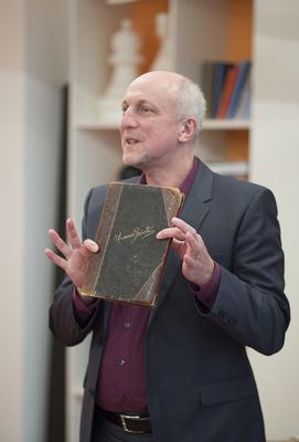Redner hält das ledergebundene Gästebuch „Unsere Gäste“ mit beiden Händen vor sich und erzählt