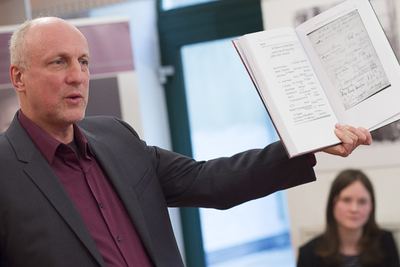 Redner hält ein aufgeschlagenes Buch mit dem Faksimile einer handschriftlichen Seite in die Höhe