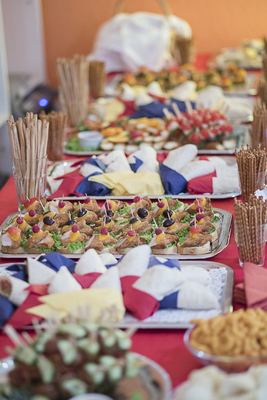 Buffet auf rotem Tischtuch mit belegten Häppchen, Salzstangen und Servietten in Blau, Weiß und Rot