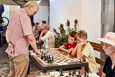 Zwei Jungen stützen nachdenklich das Kinn auf, während der Großmeister an ihrem Brett zieht