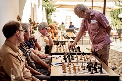 Großmeister zieht an einer langen Reihe von Simultanbrettern, die Spieler sitzen konzentriert daneben