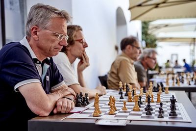 Zwei Spieler stützen sich auf den Tisch und studieren die Stellung, im Hintergrund die lange Bretterreihe