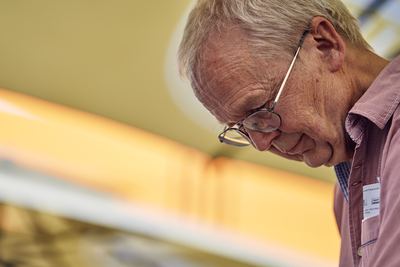 Nahaufnahme des Großmeisters mit Brille und Namensschild, den Blick konzentriert nach unten aufs Brett gerichtet