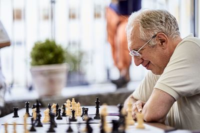 Älterer Spieler mit Brille lächelt über sein Schachbrett gebeugt, Figuren im Vordergrund unscharf