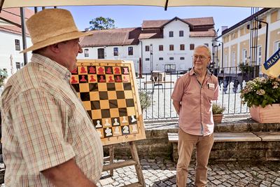 Mann mit Strohhut und Großmeister vor dem großen Demobrett, im Hintergrund die Gebäude des Klosterbauhofs