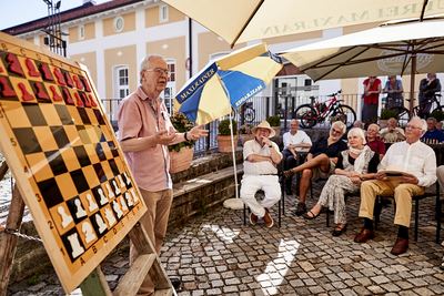 Großmeister hält am Demobrett einen Vortrag, Zuhörer sitzen im Halbkreis auf dem Pflaster des Theaterhofs