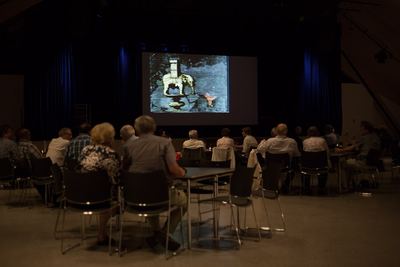 Stummfilmszene mit einer Schachfigur in Elefantenform mit Turmaufsatz auf der Leinwand, davor das Publikum im dunklen Saal