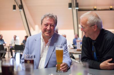 Zwei Gäste im Gespräch am Tisch, einer im hellblauen Sakko mit einem Weißbierglas vor sich